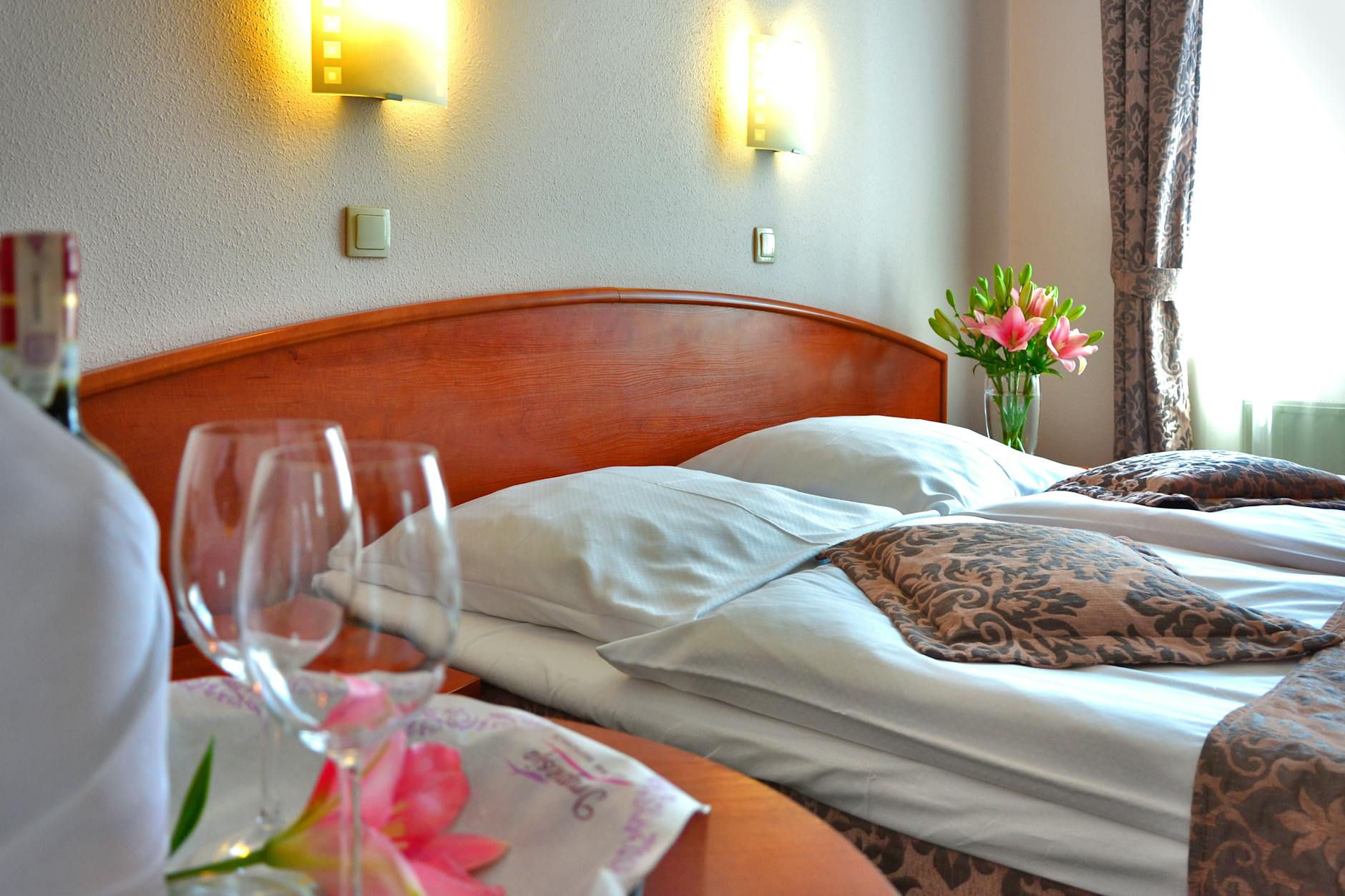 Elegancki pokój hotelowy z łóżkiem, kwiatami i kieliszkami wina
